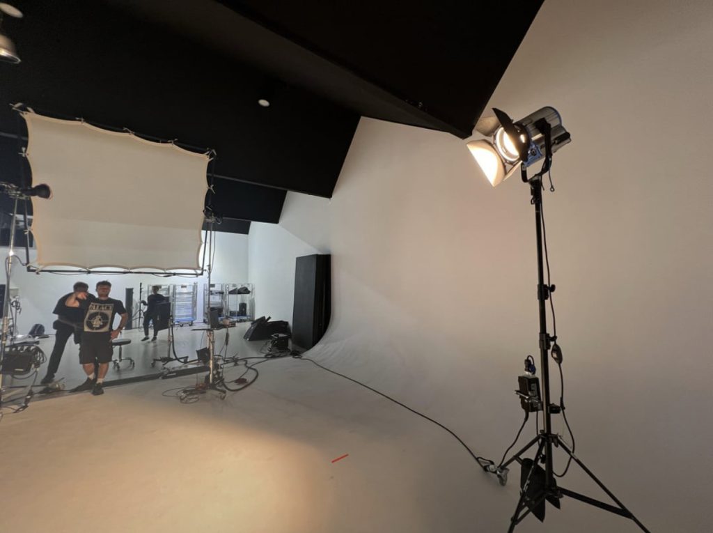 An image of a photography studio, with photography lights being shown. The studio is white and black with an angled ceiling.
